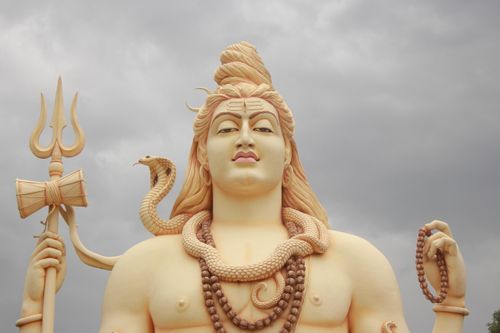 Free Close-up of a large Shiva statue under a dramatic cloudy sky, symbolizing Hinduism and spirituality. Stock Photo