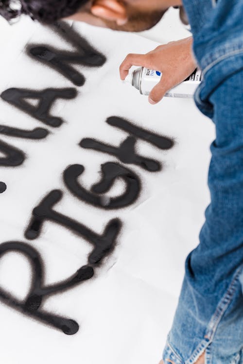 Person In Blue Denim Jeans Spray Painting The Word Human Rights
