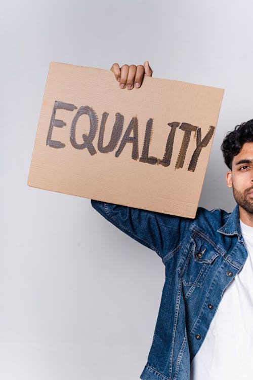Man In Blue Denim Jacket Holding Brown Cardboard With Equality Text