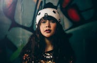 在涂鸦背景下，一位优雅的女人穿着亮片衣服，戴着时尚的白色帽子，凸显了城市时尚感