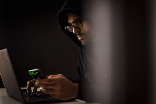 在黑暗中在筆記本電腦上打字的智能手機作物族黑客