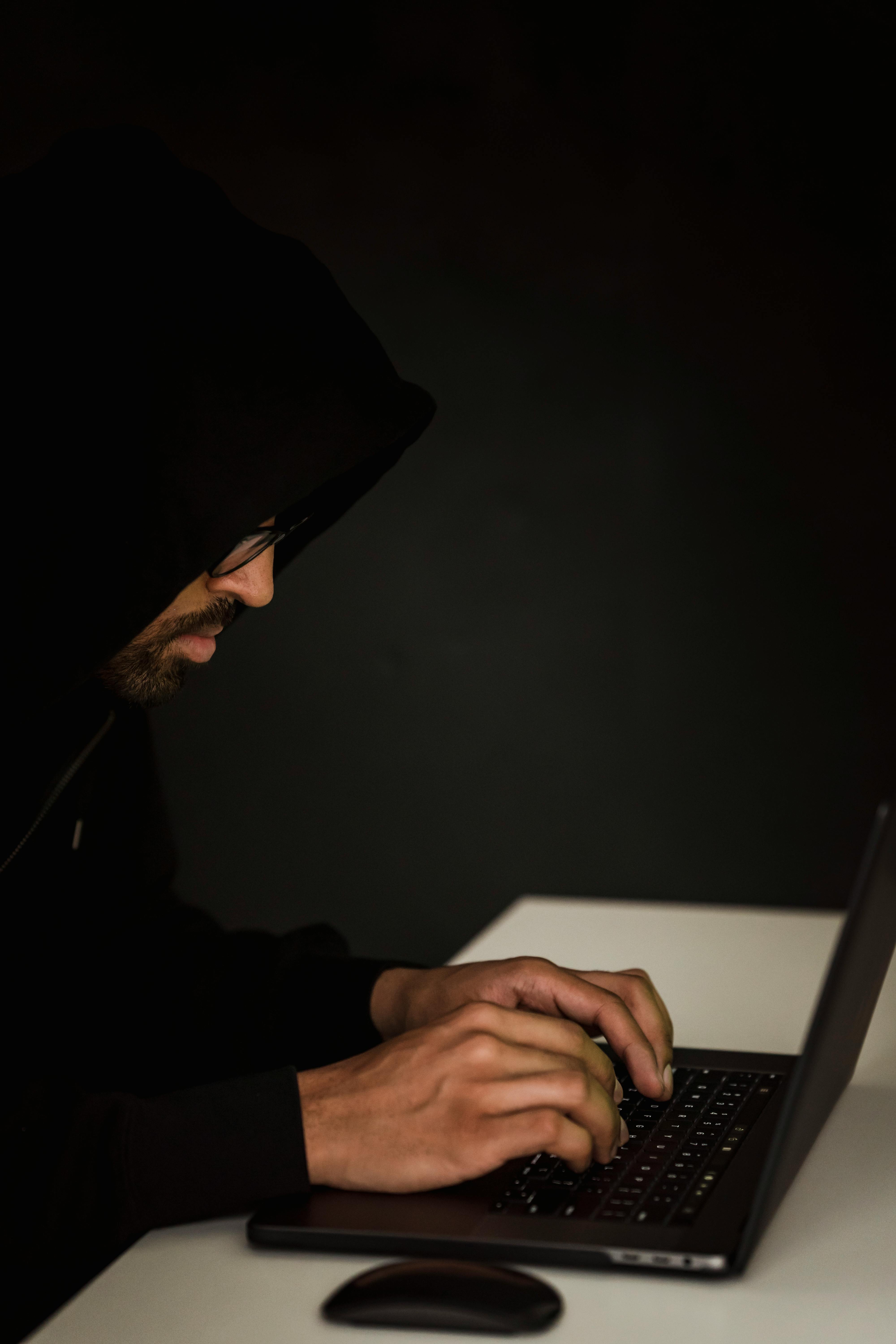 unrecognizable ethnic hacker typing on laptop at table