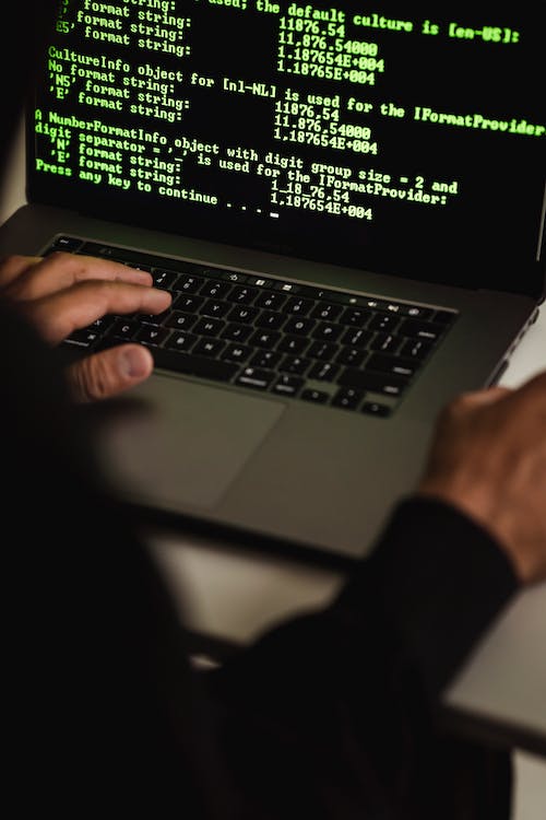 Free Crop anonymous male cyber spy hacking portable computer with codes on screen while sitting at table Stock Photo