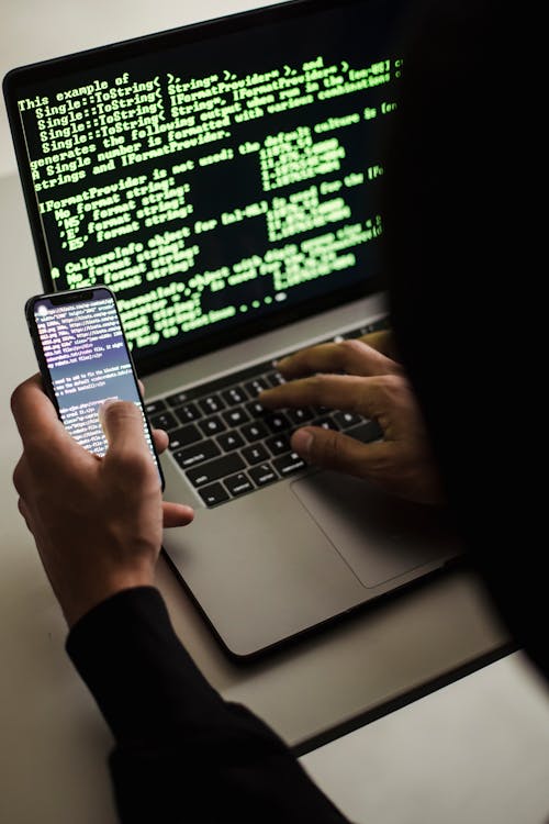 Hacker Irriconoscibile Con Smartphone Che Digita Sul Computer Portatile Alla Scrivania