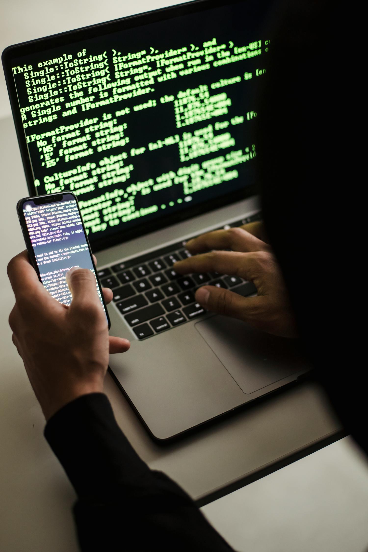 Nierozpoznany Haker Ze Smartfonem Piszącym Na Laptopie Przy Biurku