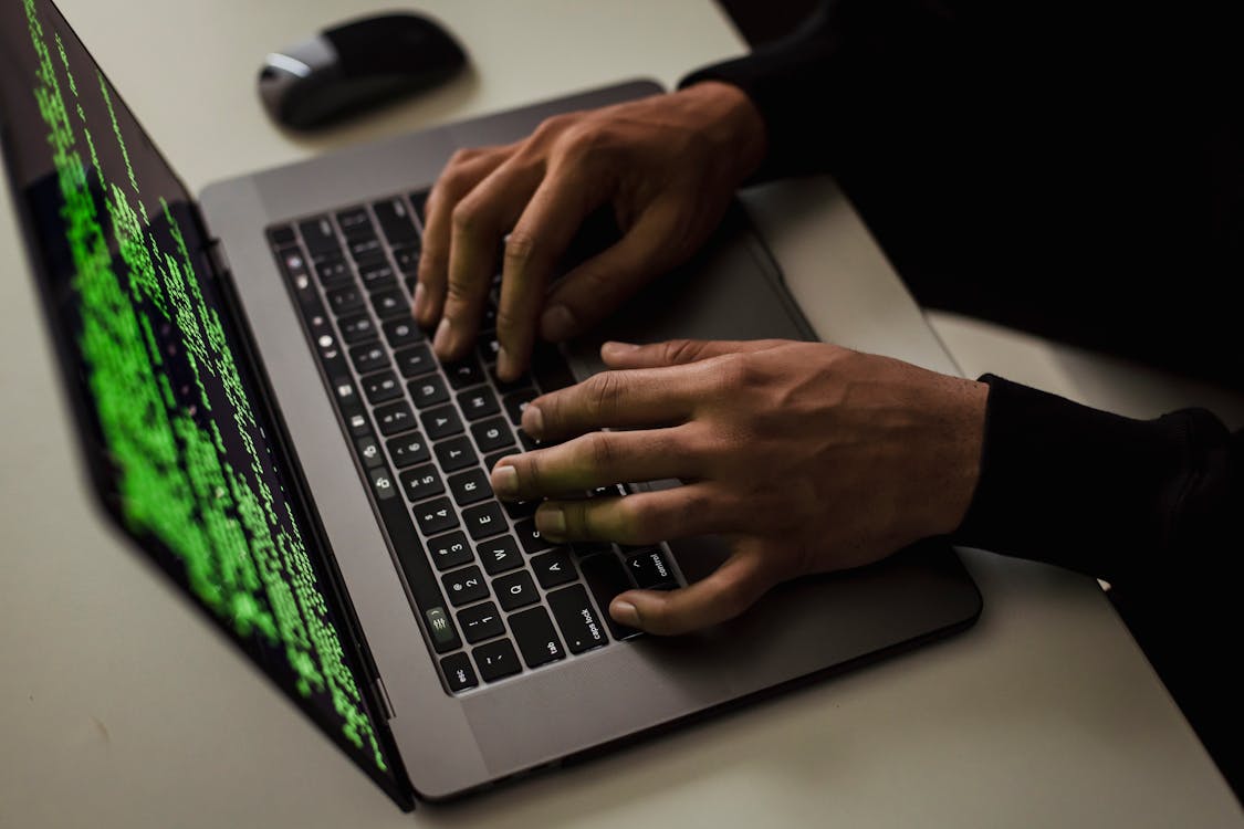 Free From above of crop anonymous male hacker typing on netbook with data on screen while sitting at desk Stock Photo