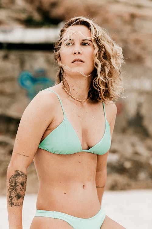 Tattooed dreamy tourist in swimwear on beach in summertime