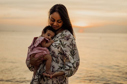 Wanita Dengan Kemeja Lengan Panjang Bunga Putih Dan Hitam Menggendong Bayi Dengan Kemeja Pink