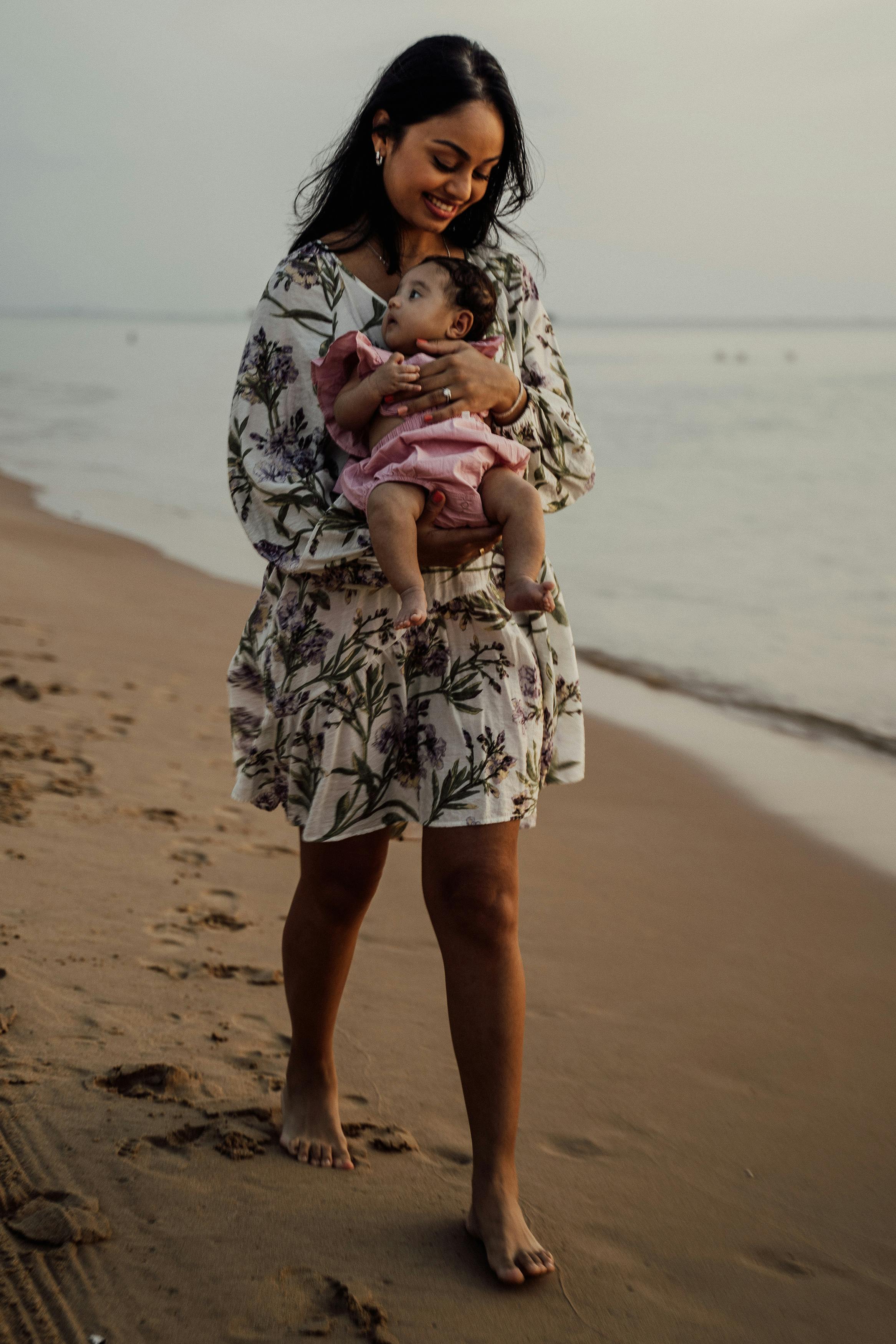 a woman carrying a child while walking beside the beach