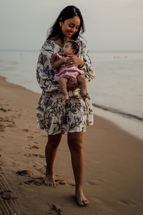 Free A Woman CArrying a Child while Walking Beside the Beach Stock Photo