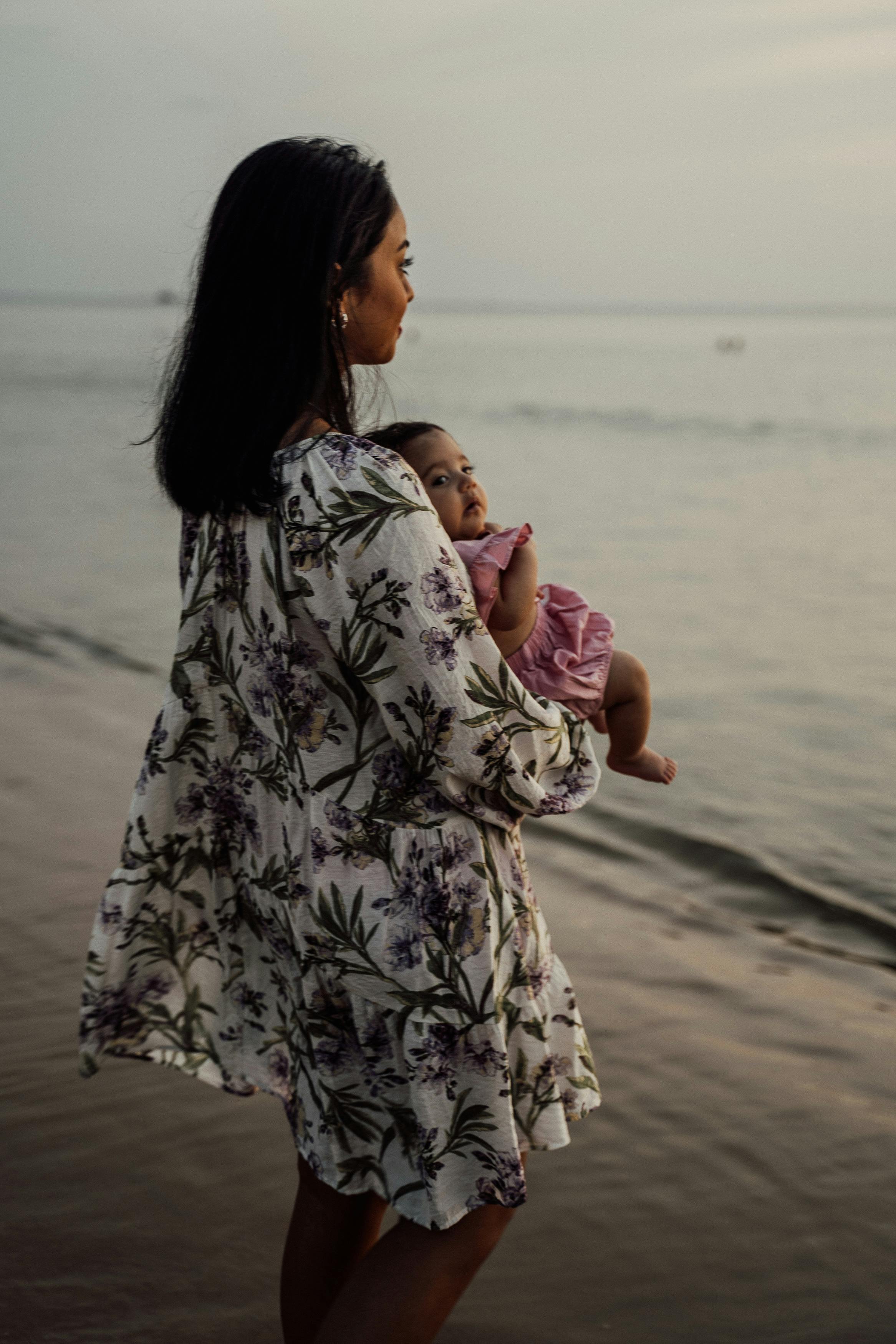 woman standing in the seashore carrying her precious baby