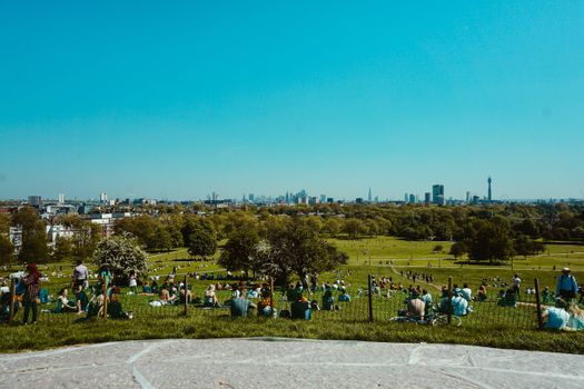A scenic view from Primrose Hill with people relaxing and London skyline in the background.