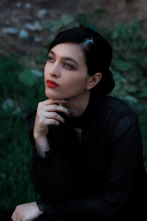 Stylish woman touching face and sitting on lawn