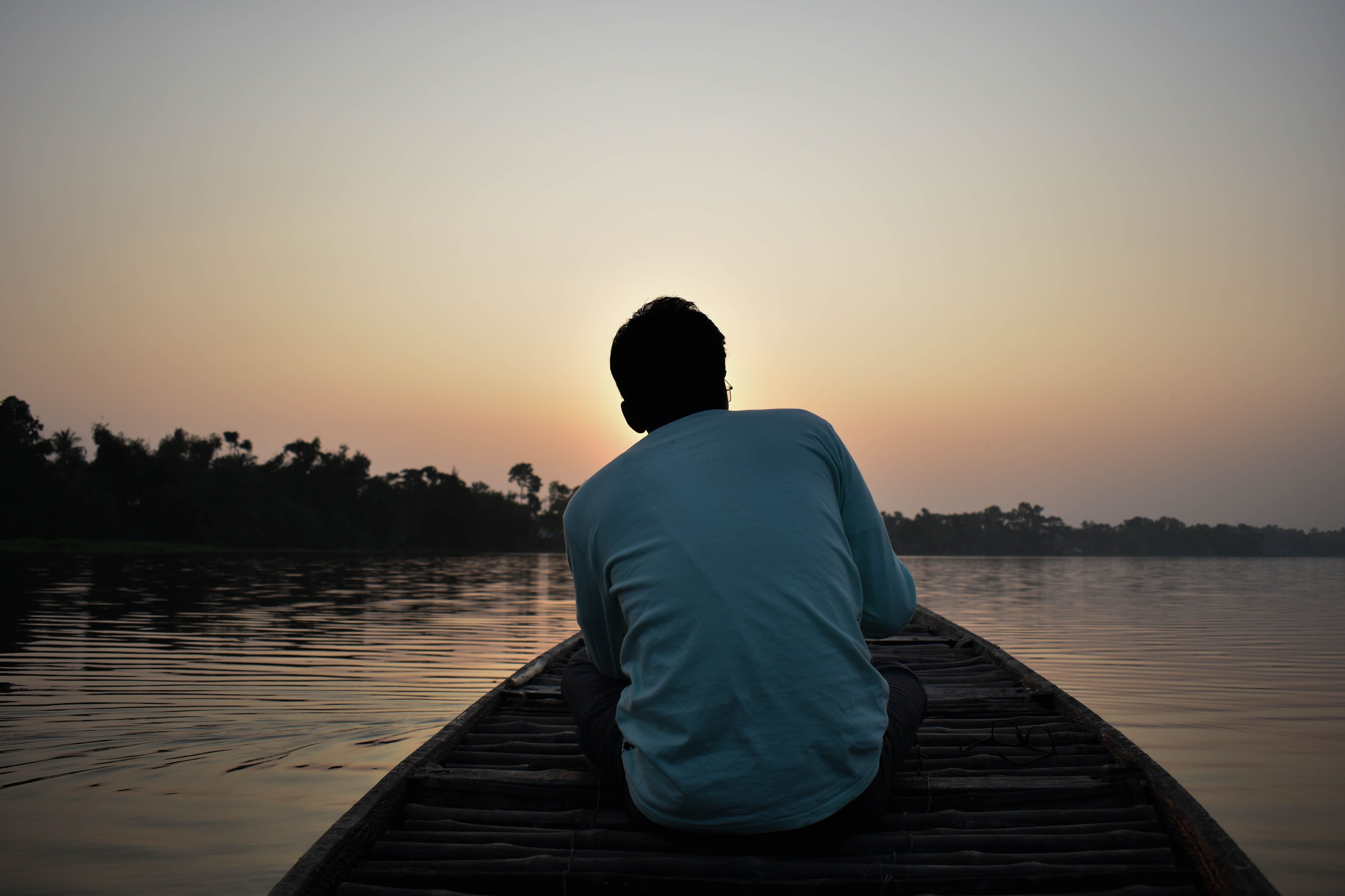 Silhouette of a man sitting in a boat during dawn on a calm river, capturing solitude.