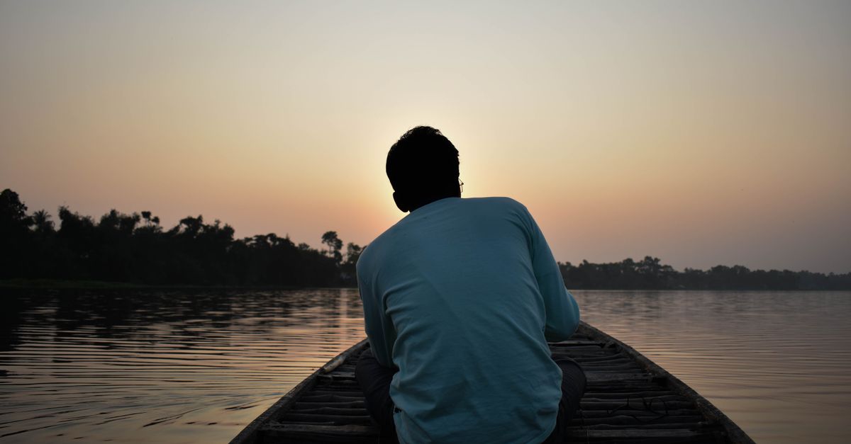 Silhouette of a man sitting in a boat during dawn on a calm river, capturing solitude.