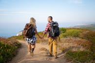 一对夫妇手牵着手，背着背包沿着葡萄牙乡村风景秀丽的海滨小径徒步旅行