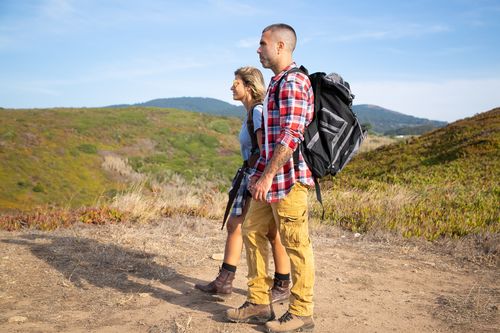 Free Couple hiking in Portugal's lush landscape with backpacks under a clear blue sky. Stock Photo