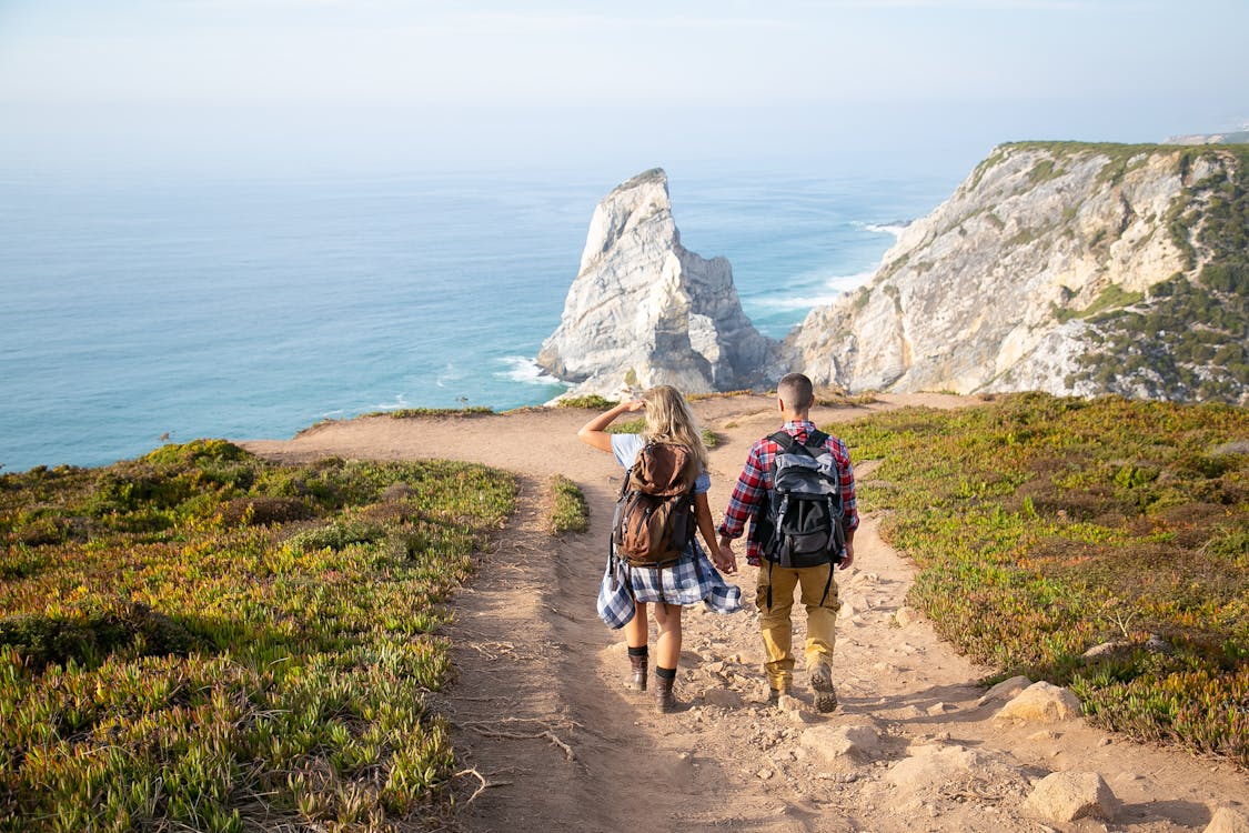 Man in Black Shirt and Black Shorts Carrying Hiking Backpack Walking on Pathway Near Body of Near Near Near Near