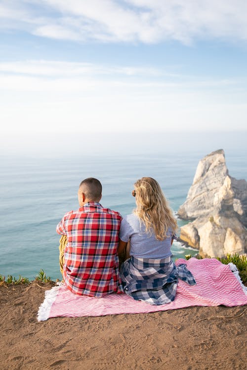Back View Shot of Man and Woman Sitting on the Cliff of a Mountain