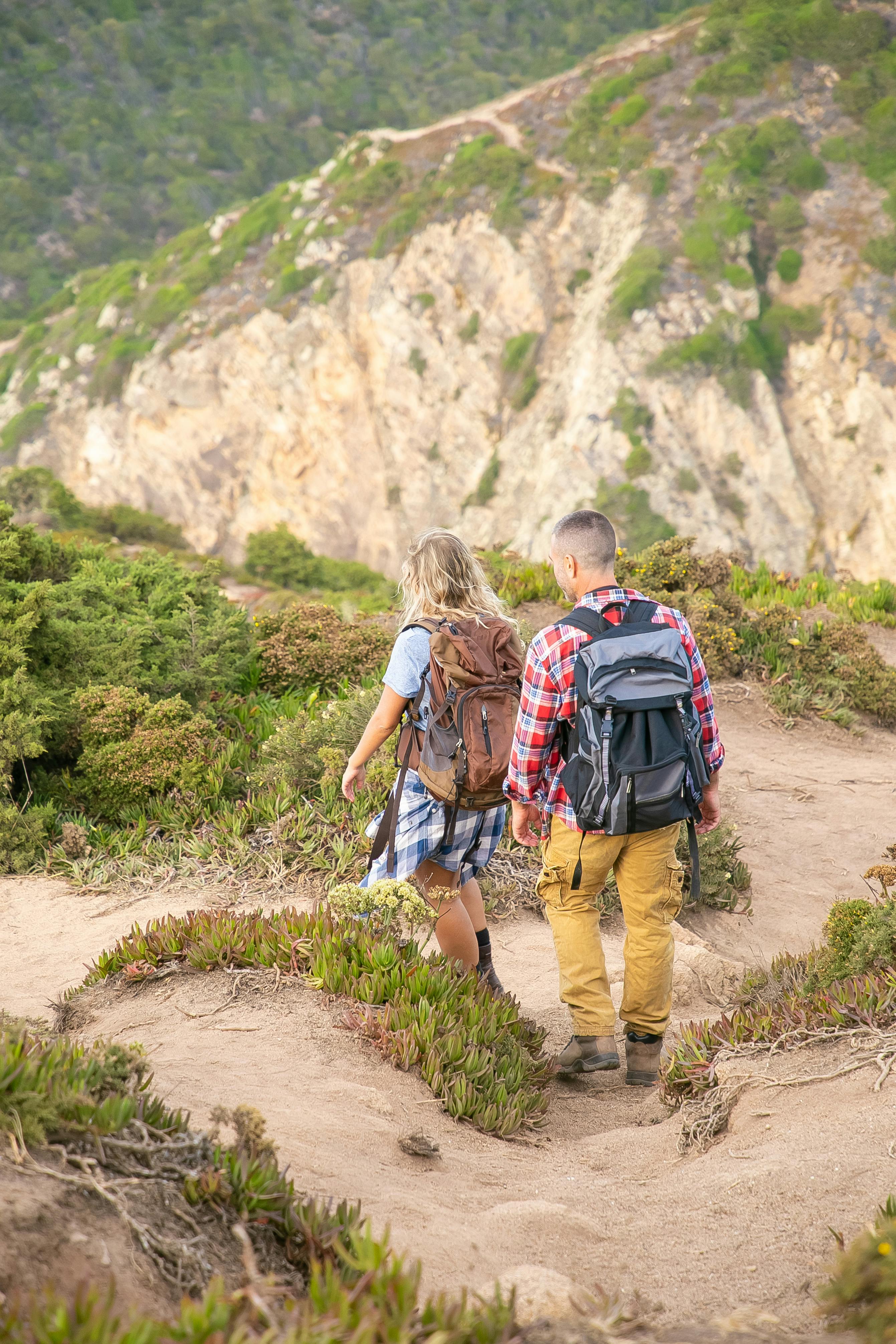 两名徒步旅行者正沿着葡萄牙一条风景优美的山间小道前行，四周环绕着郁郁葱葱的绿植和陡峭的悬崖