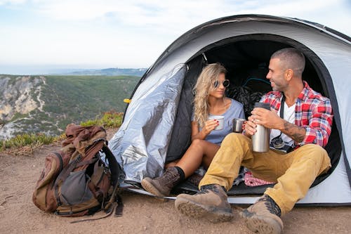 A Couple Sitting Inside the Tent Holding Mugs while Looking at Each Other