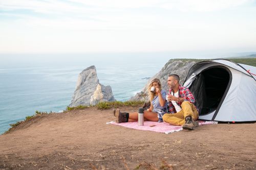 Free A couple enjoys a scenic cliffside camping experience with a tent and ocean view. Stock Photo