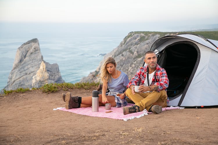 Man And Woman Resting On A Mountain Top While Eating Snacks