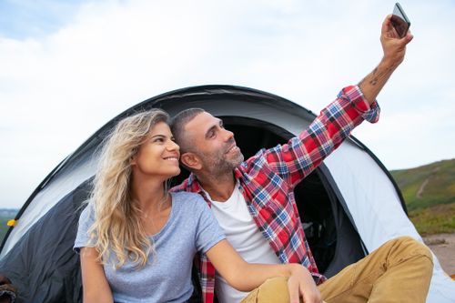 Free Happy couple enjoying a camping trip, taking selfies outside their tent. Stock Photo