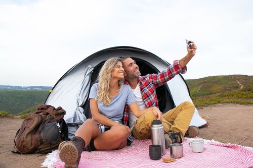 Free Happy couple enjoying a camping trip, taking a selfie in front of a tent with scenic views. Stock Photo