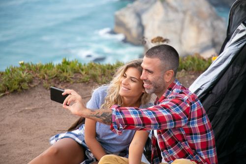 Free Happy couple taking a selfie by a tent on a picturesque cliff in Portugal. Stock Photo