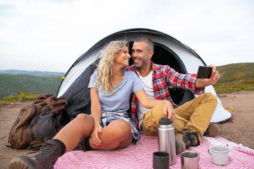 Free Smiling couple camping outdoors taking selfie with phone. Enjoying nature and togetherness. Stock Photo