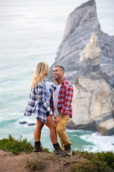 A couple standing happily on a cliff overlooking the Portuguese seascape, embracing nature's beauty.