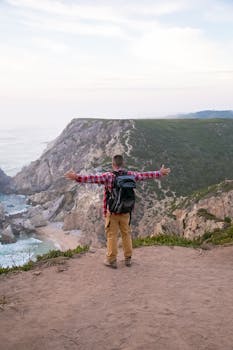 Man with backpack embraces stunning ocean view from Portugal's cliffs. Perfect for travel and nature themes.