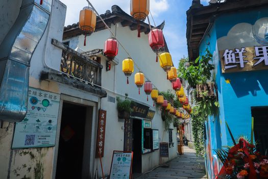 Vibrant lanterns hang over a narrow street lined with traditional houses, creating a picturesque scene.