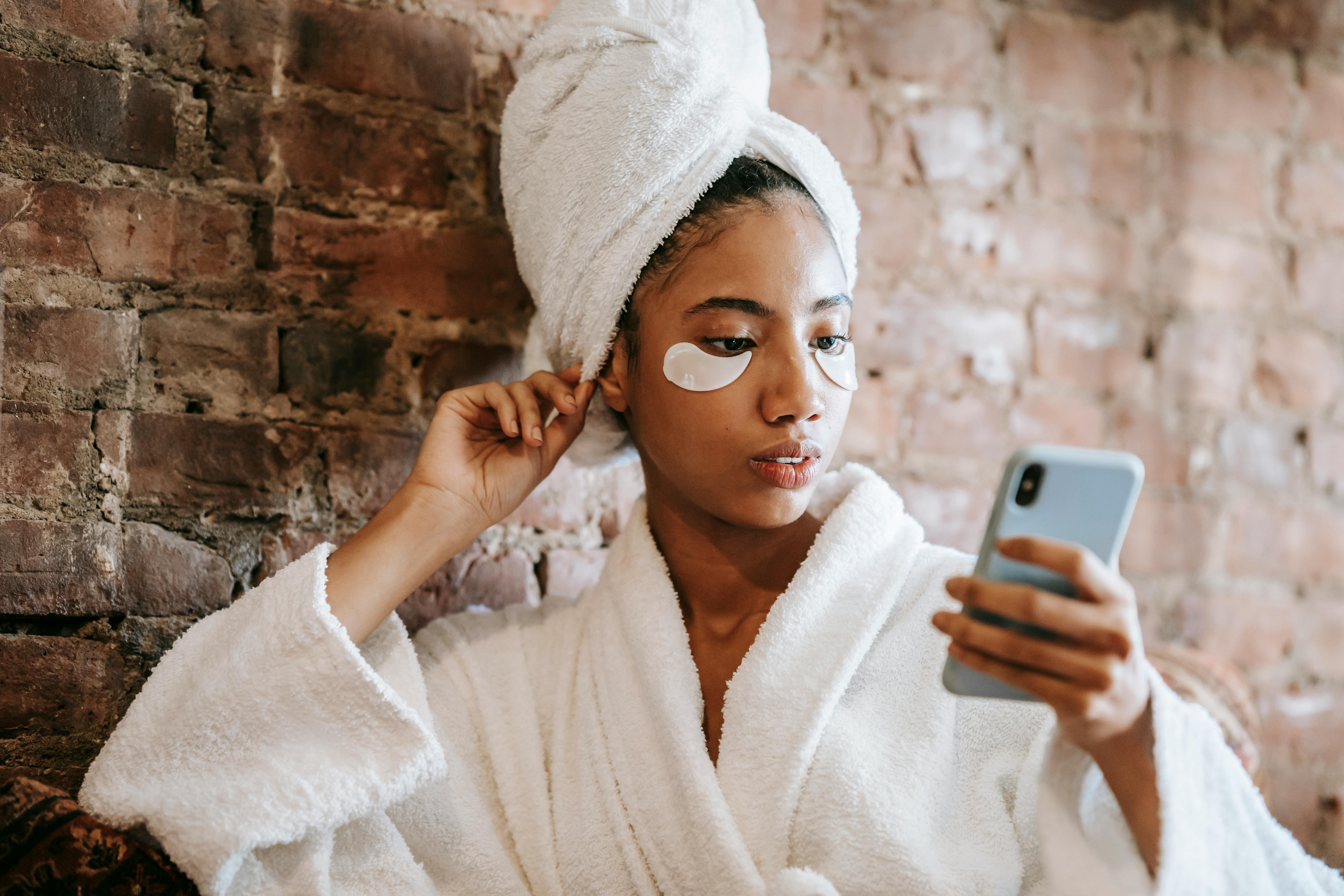 ethnic woman in eye patches watching smartphone in spa salon