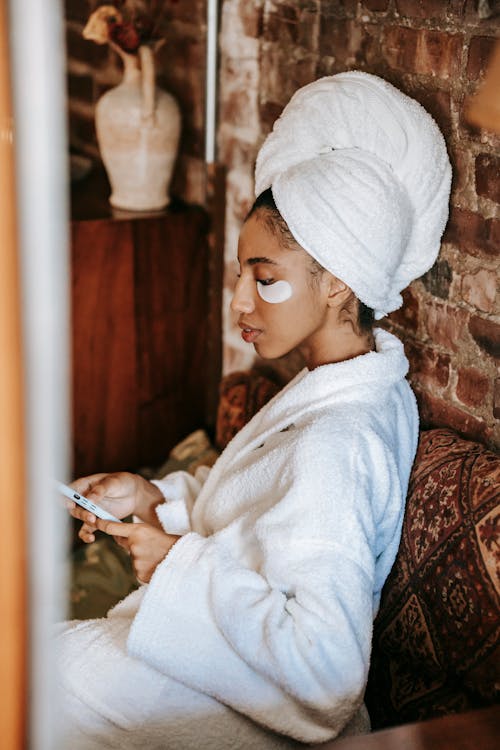 Free Ethnic woman in robe surfing internet on smartphone in salon Stock Photo