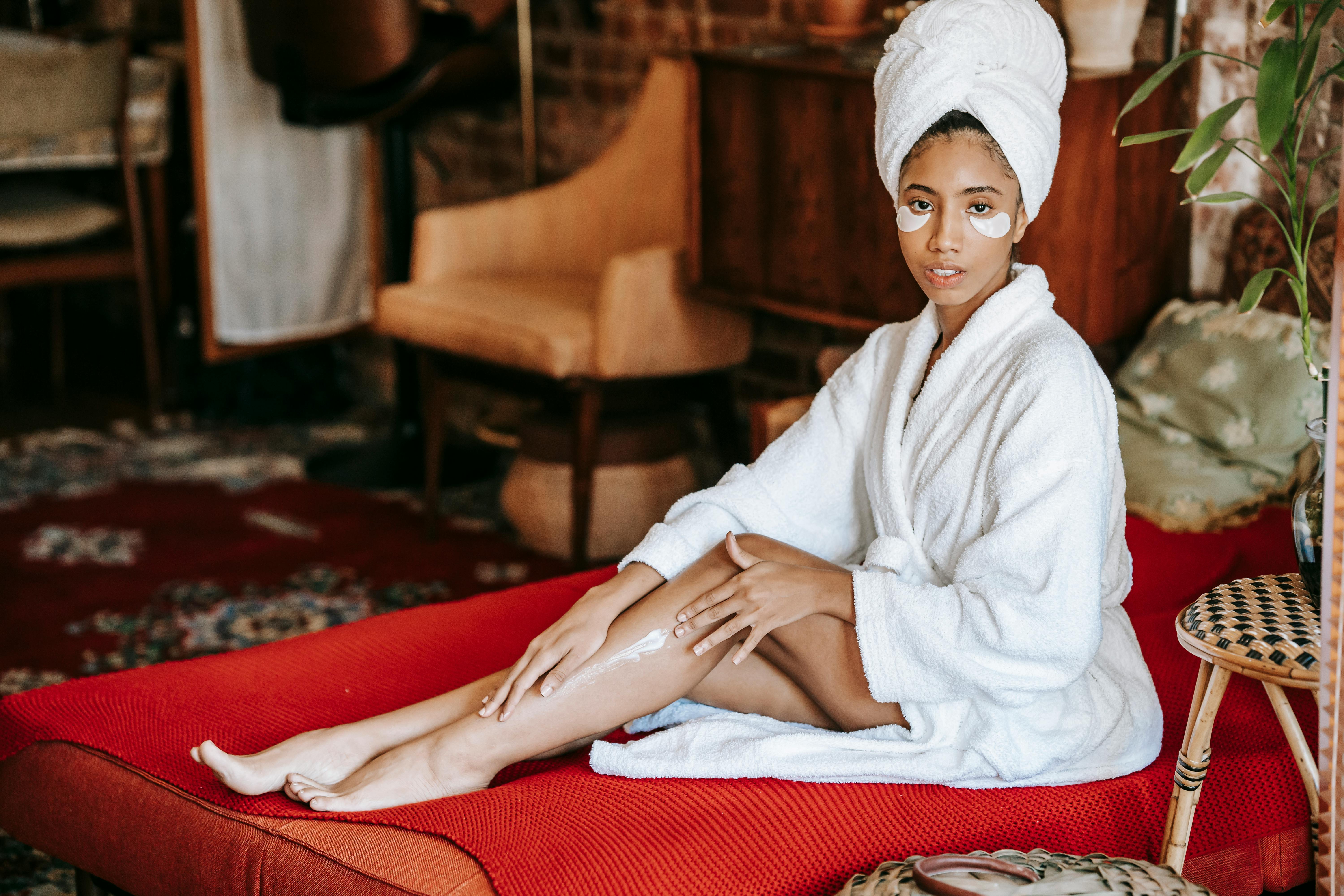 relaxed ethnic woman with eye patches applying cream on leg