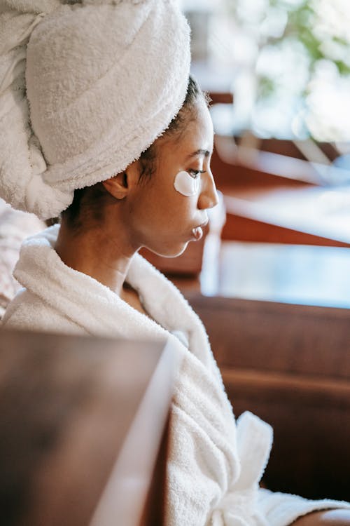Side view of young ethnic female with terry towel on head resting in beauty salon during facial procedure