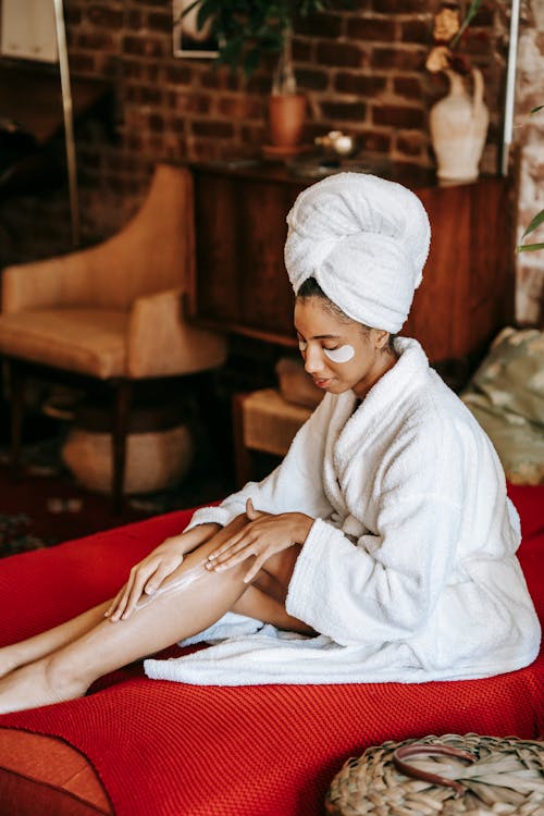 Relaxed young black woman applying cream on body after shower