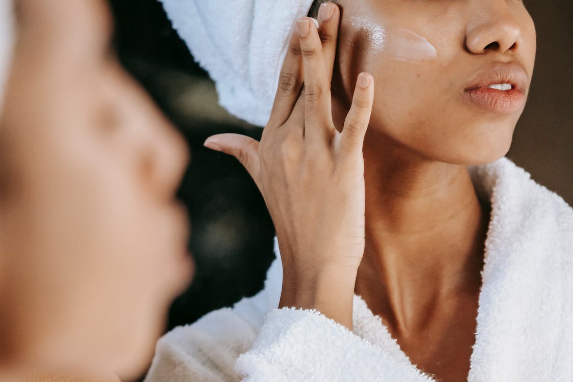 Gratis Mujer étnica De Cultivo Aplicando Crema En La Cara Contra El Espejo Foto de stock