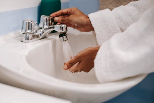 A woman in a robe washing her hands under running water in a bathroom sink, highlighting hygiene and wellness.