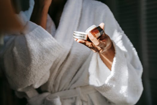 A woman in a white robe holding skincare products, enjoying a tranquil morning routine.