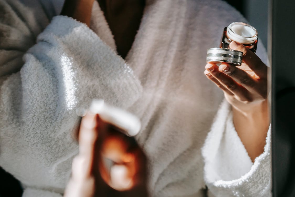 Crop ethnic woman with jar of cream against mirror