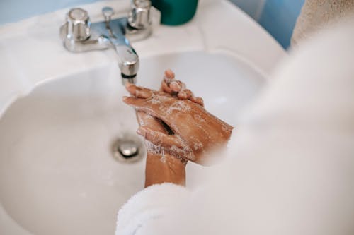 From above of crop unrecognizable ethnic female in robe washing hands with soap in bathroom