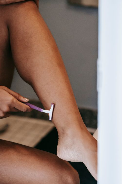 Free Crop anonymous barefoot ethnic female shaving leg with disposable razor during daily routine in bathroom Stock Photo