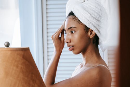 Charming ethnic woman cleaning face with cotton pad at home