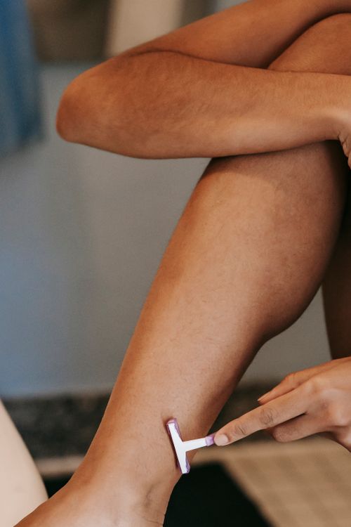 Free Crop anonymous ethnic female with delicate skin depilating leg with disposable razor in bathroom in house Stock Photo