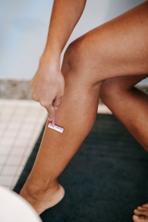 種族的女人用剃刀在浴室剃須腿