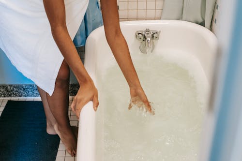 Ethnic woman pouring water into bath for morning routine
