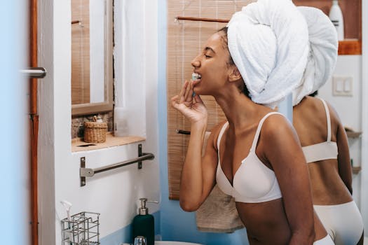 A young woman in a bathroom flossing her teeth with a towel wrapped around her head, promoting oral hygiene.